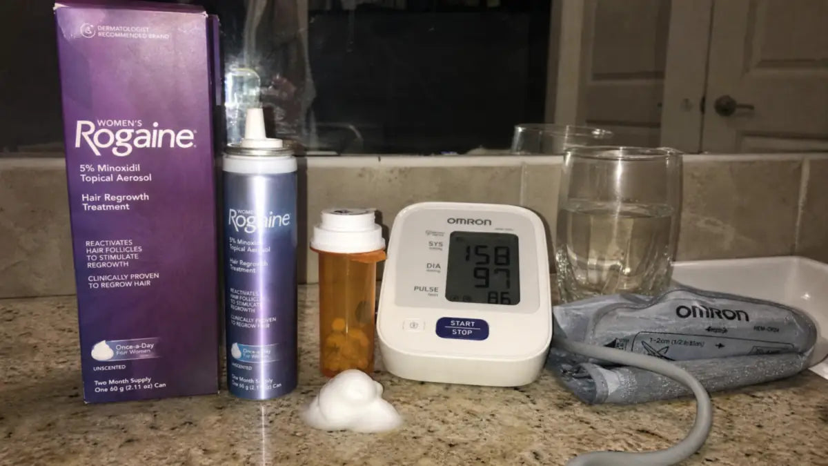 Women’s Rogaine minoxidil foam next to prescription pills and a blood pressure monitor